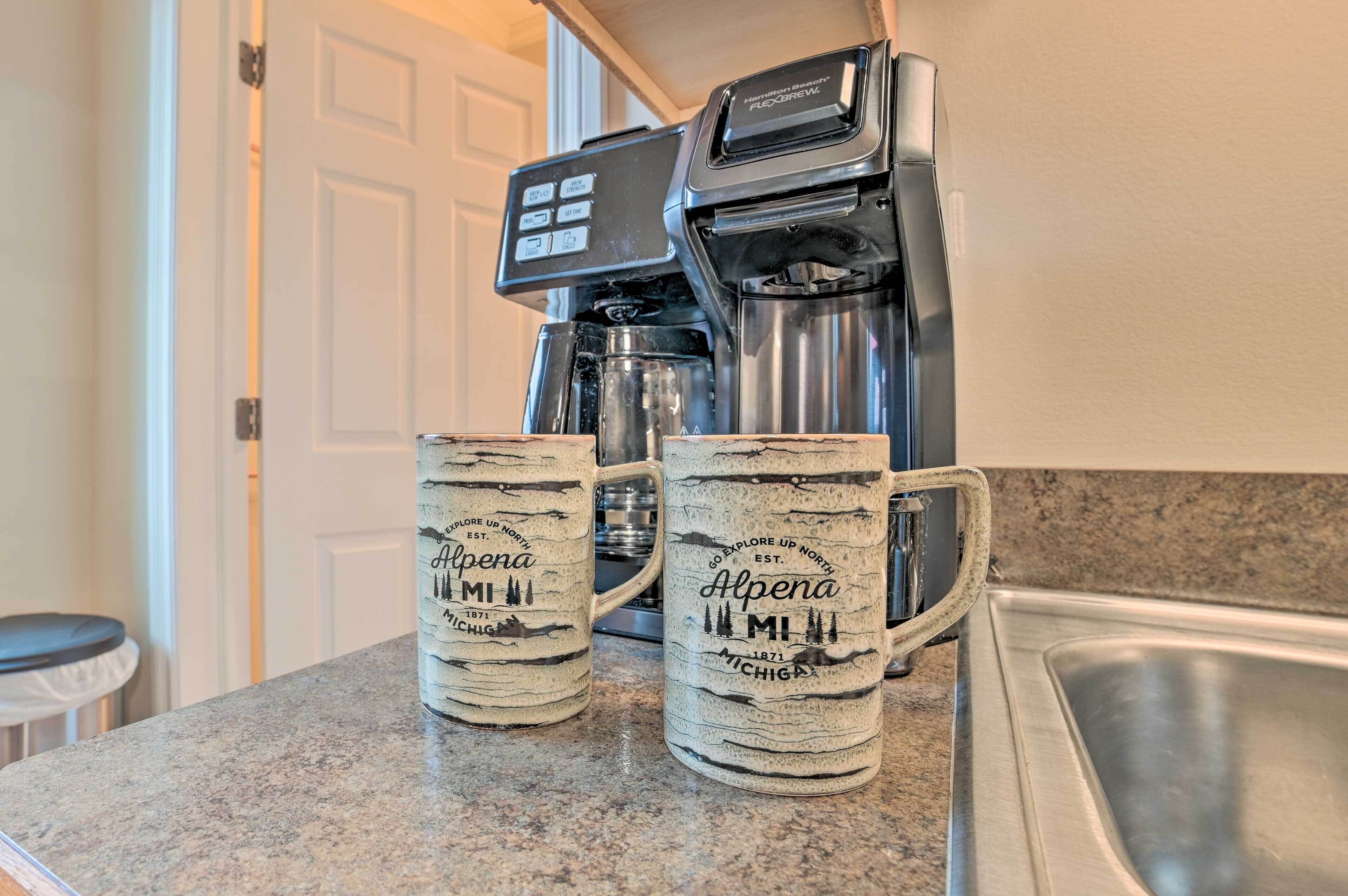 Dos tazas de café sobre una encimera de cocina, con una cafetera al fondo.