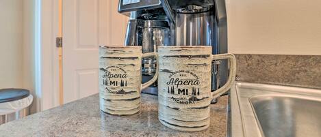 Dos tazas de café sobre una encimera de cocina, con una cafetera al fondo.
