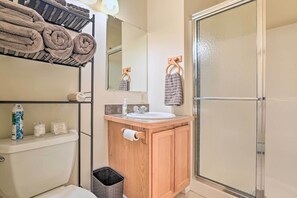 A bathroom with a wooden vanity, a toilet, a sink, a mirror, and a glass shower enclosure. - Downtown Loft Apartment, Steps to Riverfront! (Alpena)