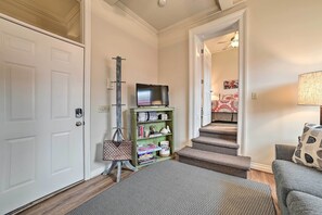 A hallway with a door, a coat rack, a television on a stand, a green shelf with books, and a staircase leading to another room. - Downtown Loft Apartment, Steps to Riverfront! (Alpena)
