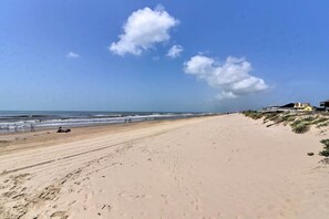 A wide sandy beach with a clear sky and a few clouds. There are buildings on the right side of the beach. - Deck & Grill: Walkable Crystal Beach House! (Port Bolivar)