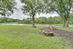 Une zone herbeuse avec une rivière, des arbres et une pile de bois de chauffage.
