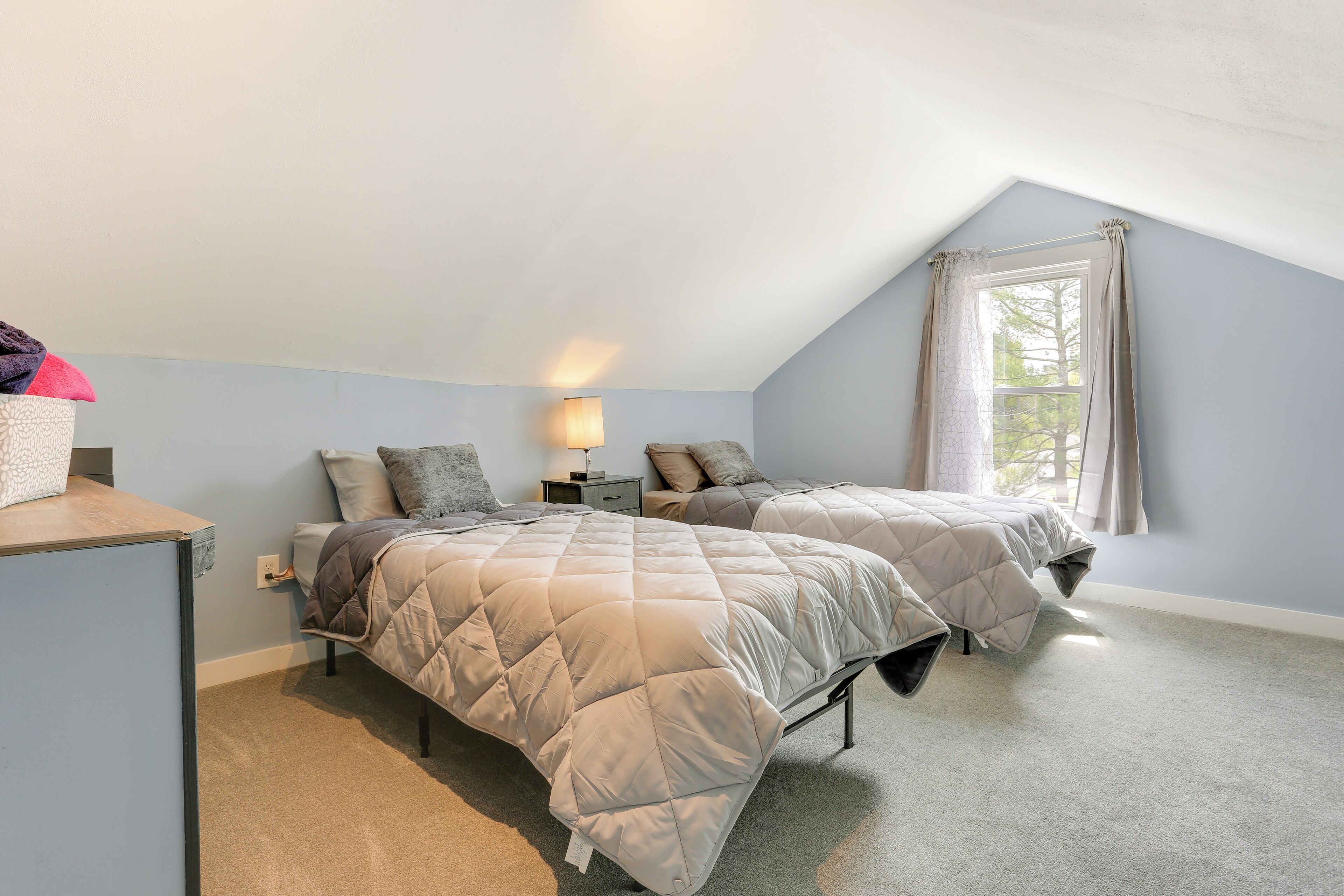 A bedroom with two beds, a desk, a lamp, and a window with curtains.