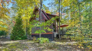 Une cabane dotée d’une véranda et d’un escalier, entourée d’arbres et d’une terrasse en bois.
