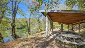 Un abri en bois, équipé de bancs et de tables, situé au bord d’un lac entouré d’arbres.
