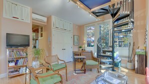Un salon chaleureux avec un téléviseur, des étagères à livres, des fauteuils en osier, une table basse et un escalier en colimaçon.