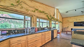 A modern kitchen with wooden cabinets, a granite countertop, and large windows offering a view of a forested landscape. - Direct Hiking Access: Riverfront Dolores Home! (Dolores)