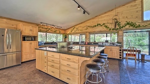 A spacious kitchen with wooden cabinets, a large island with stools, and a view of the outdoors through large windows. - Direct Hiking Access: Riverfront Dolores Home! (Dolores)