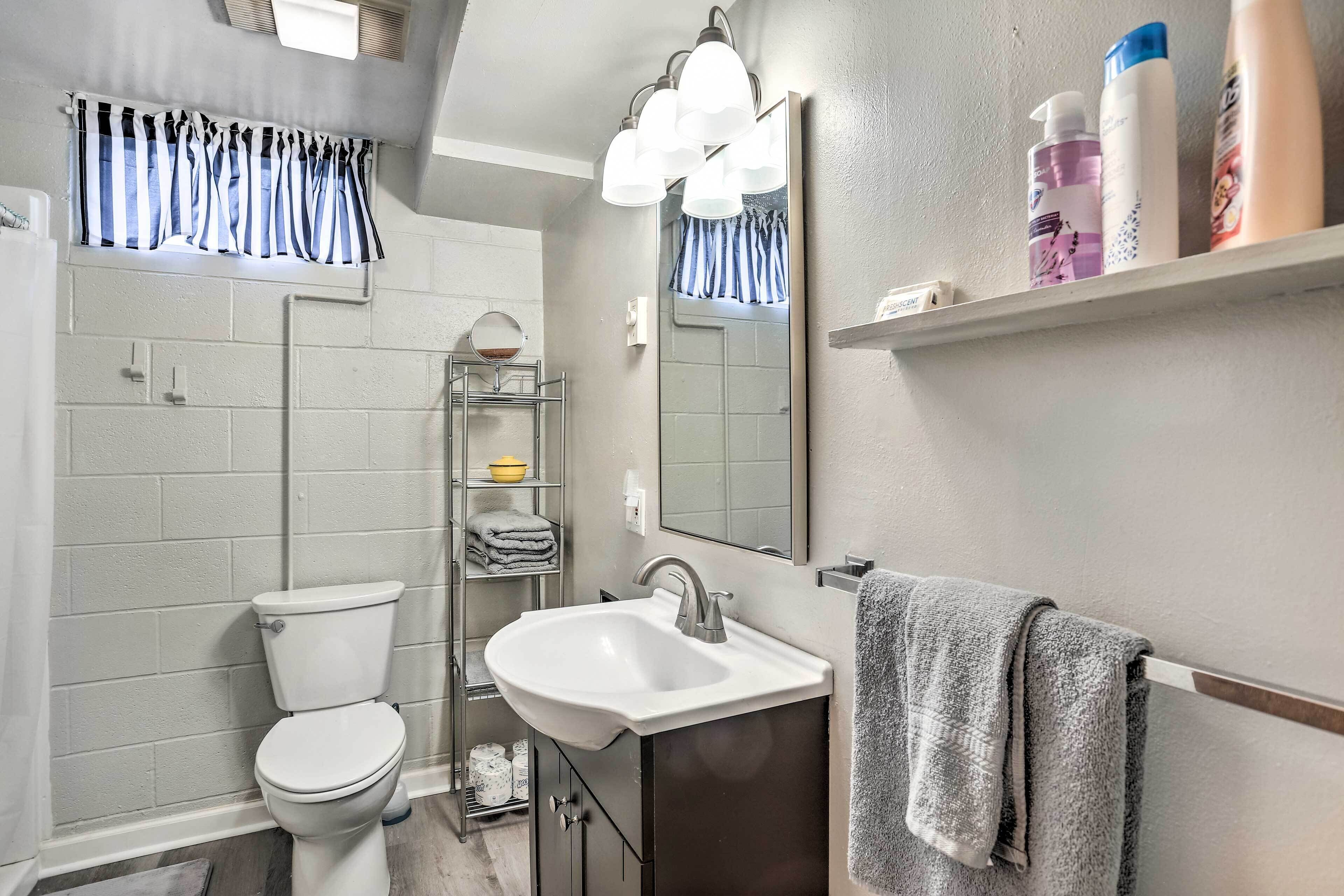 A bathroom with a toilet, sink, mirror, and shelves with toiletries.