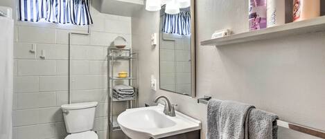A bathroom with a toilet, sink, mirror, and shelves with toiletries.