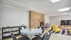 A modern living room with a brick fireplace, a round glass table with chairs, a TV, and a wooden cabinet.