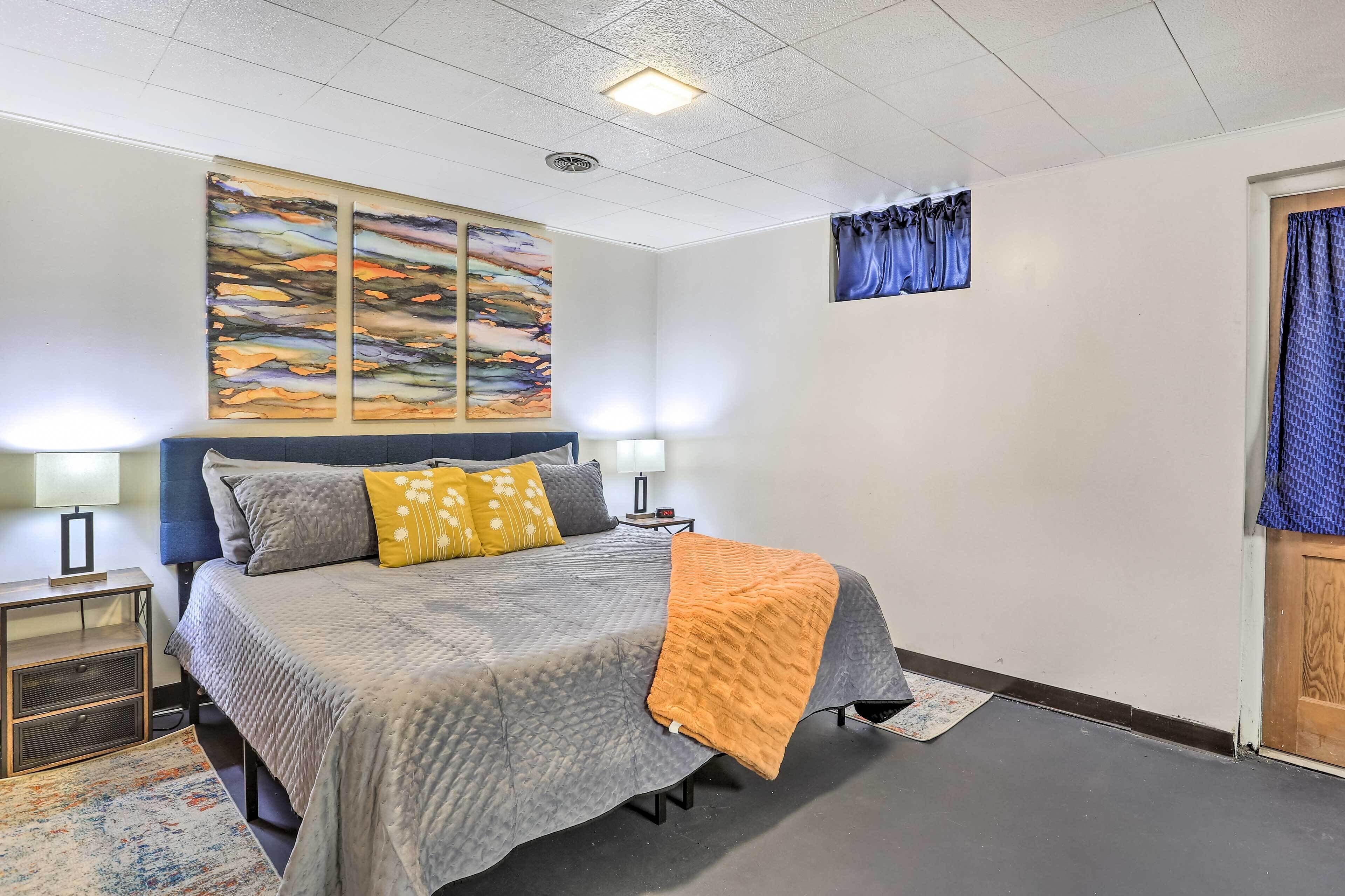 A bedroom with a bed, two bedside tables, a nightstand, a rug, and artwork on the wall.