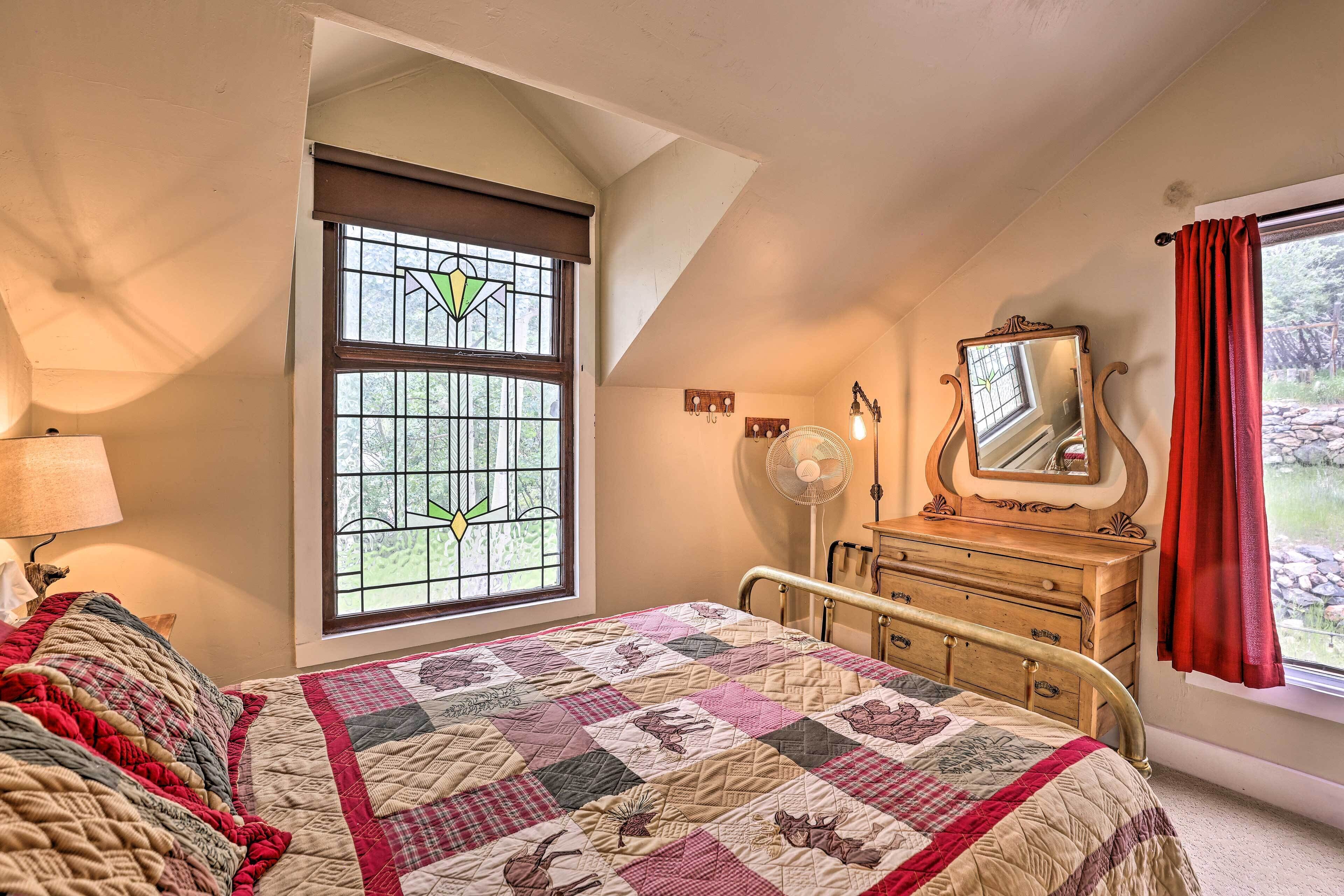 Une chambre à coucher avec un lit, une commode, un miroir, une fenêtre avec des rideaux et un ventilateur.