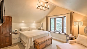 A bedroom with a large bed, a wooden chest, a bench, a nightstand, a lamp, and a window with curtains. - Family Home in Georgetown: Walk to Town & Railroad (Georgetown)