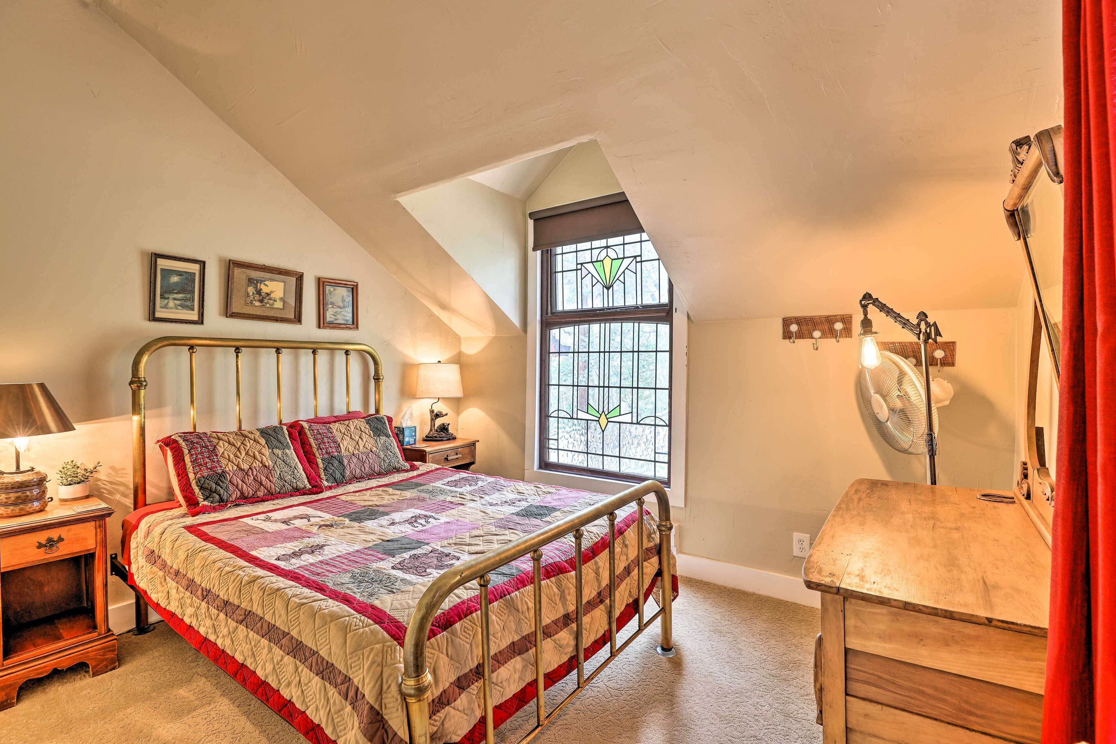 A bedroom with a bed, a nightstand, a dresser, a window with a view, and a ceiling fan.