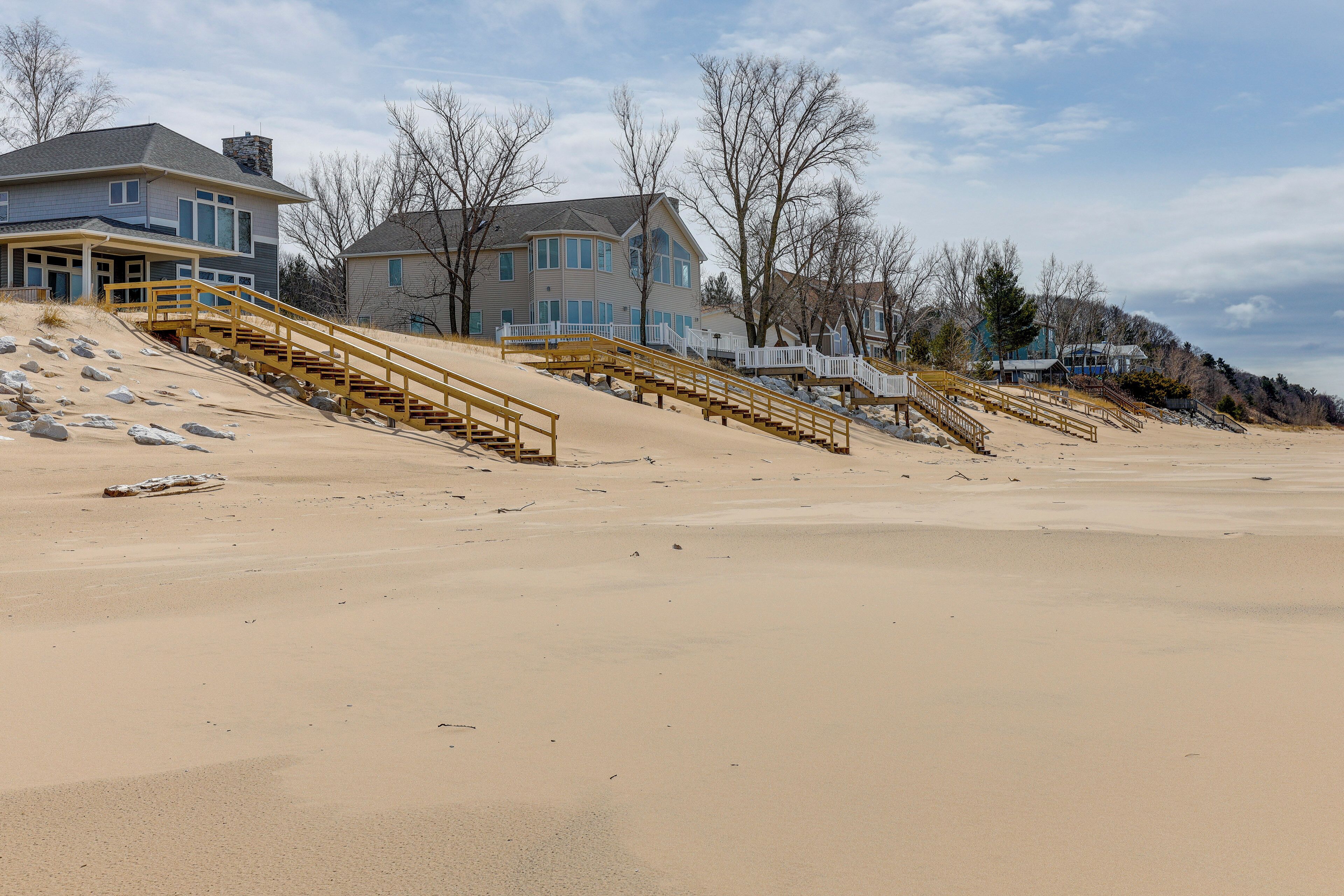 A beachfront property with multiple houses, sandy beach, and wooden staircases leading to the beach.