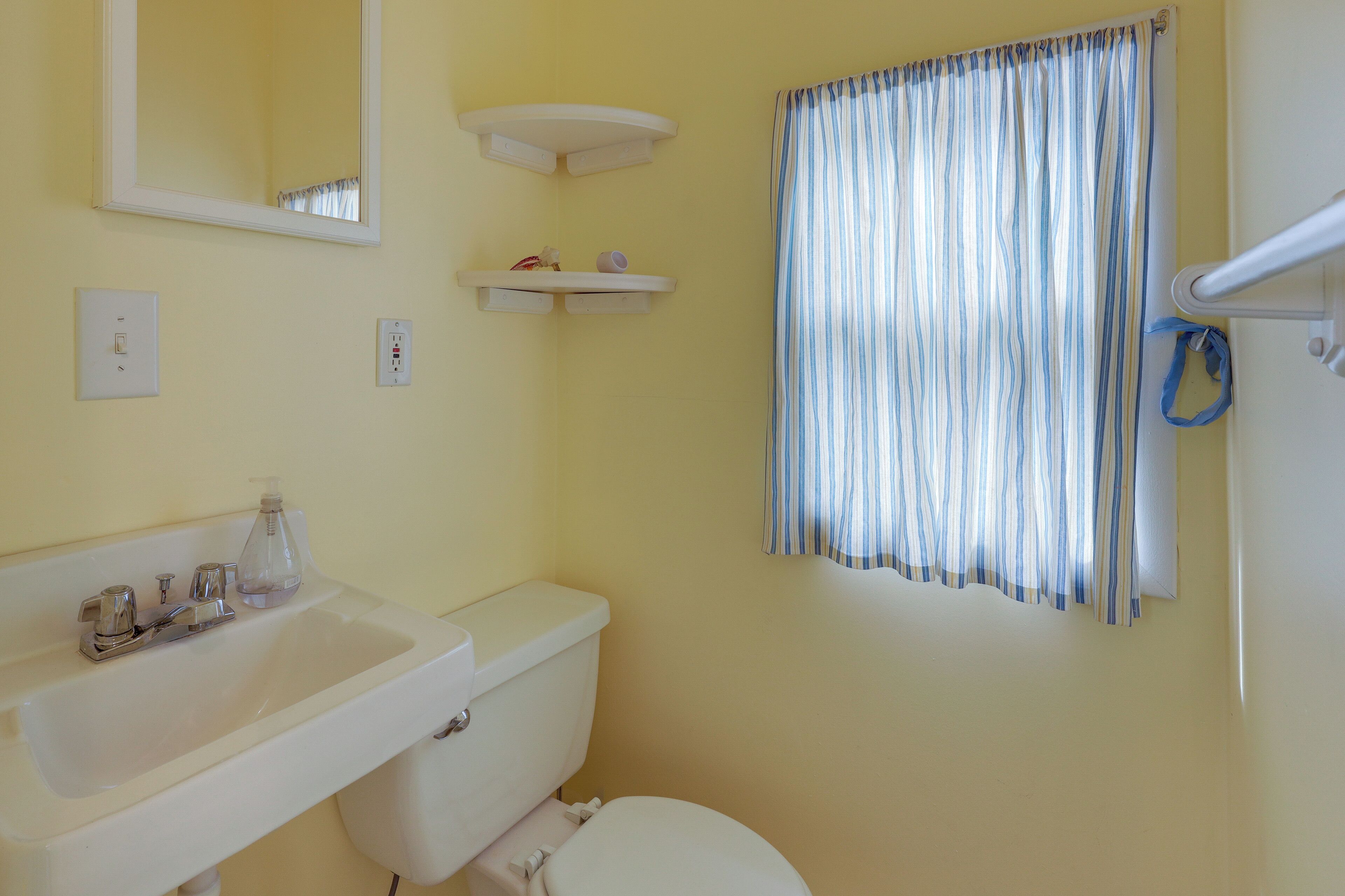 A bathroom with a white sink, mirror, toilet, and striped shower curtain.