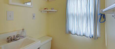 A bathroom with a white sink, mirror, toilet, and striped shower curtain.