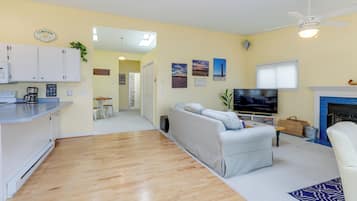 A living room with a sofa, TV, and fireplace. There is a kitchen area with cabinets and a countertop.