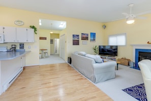A living room with a sofa, TV, and fireplace. There is a kitchen area with cabinets and a countertop. - Family Friendly Mears Cottage - Walk to the Beach! (Mears)