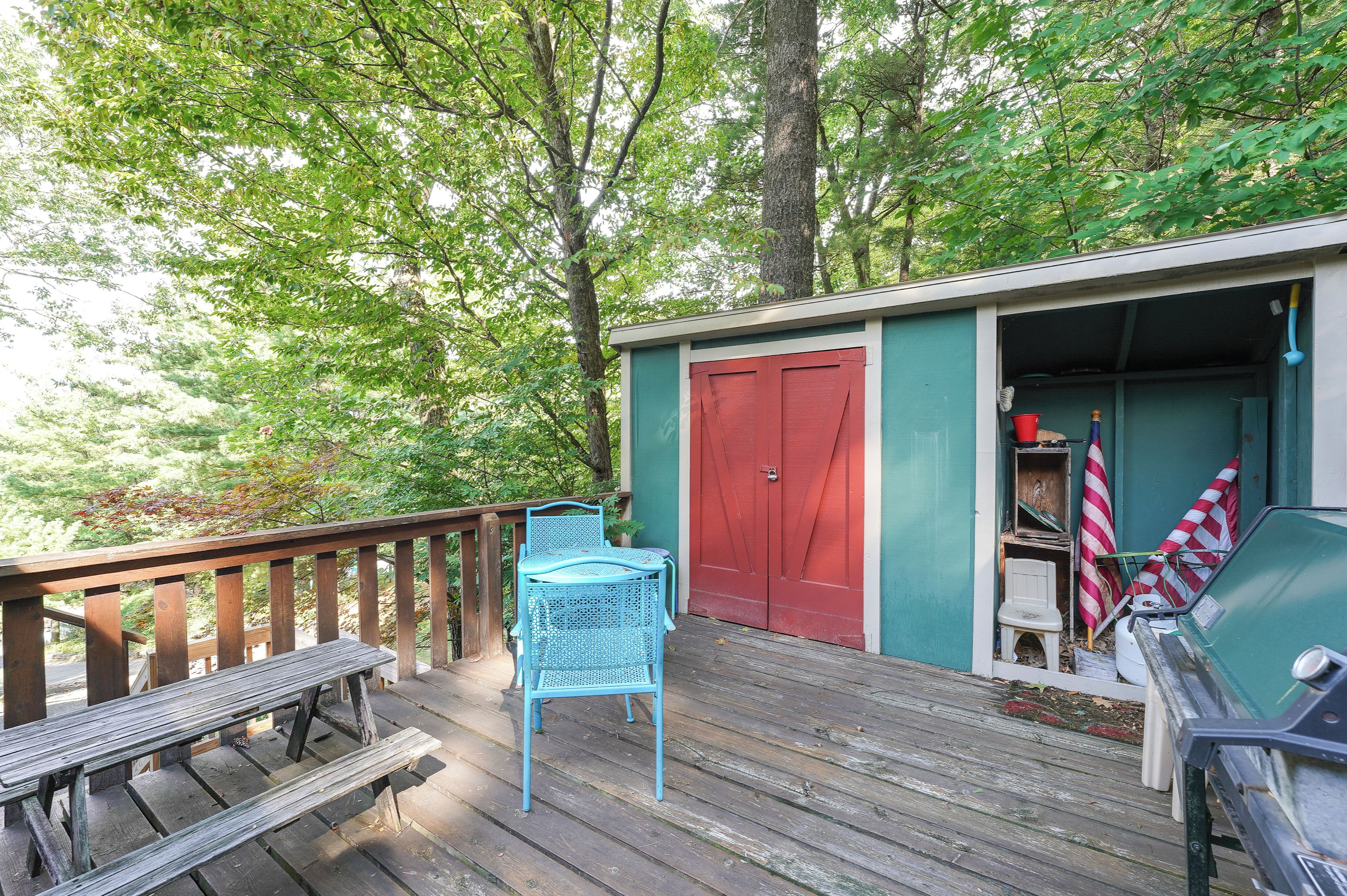 Eine Holzterrasse mit Tisch und Stühlen, eine rote Tür und ein kleines Gartenhaus mit darin befindlichen Gegenständen.