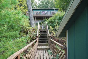 A wooden staircase leading to a building with a green exterior, surrounded by dense greenery. - Family Friendly Mears Cottage - Walk to the Beach! (Mears)