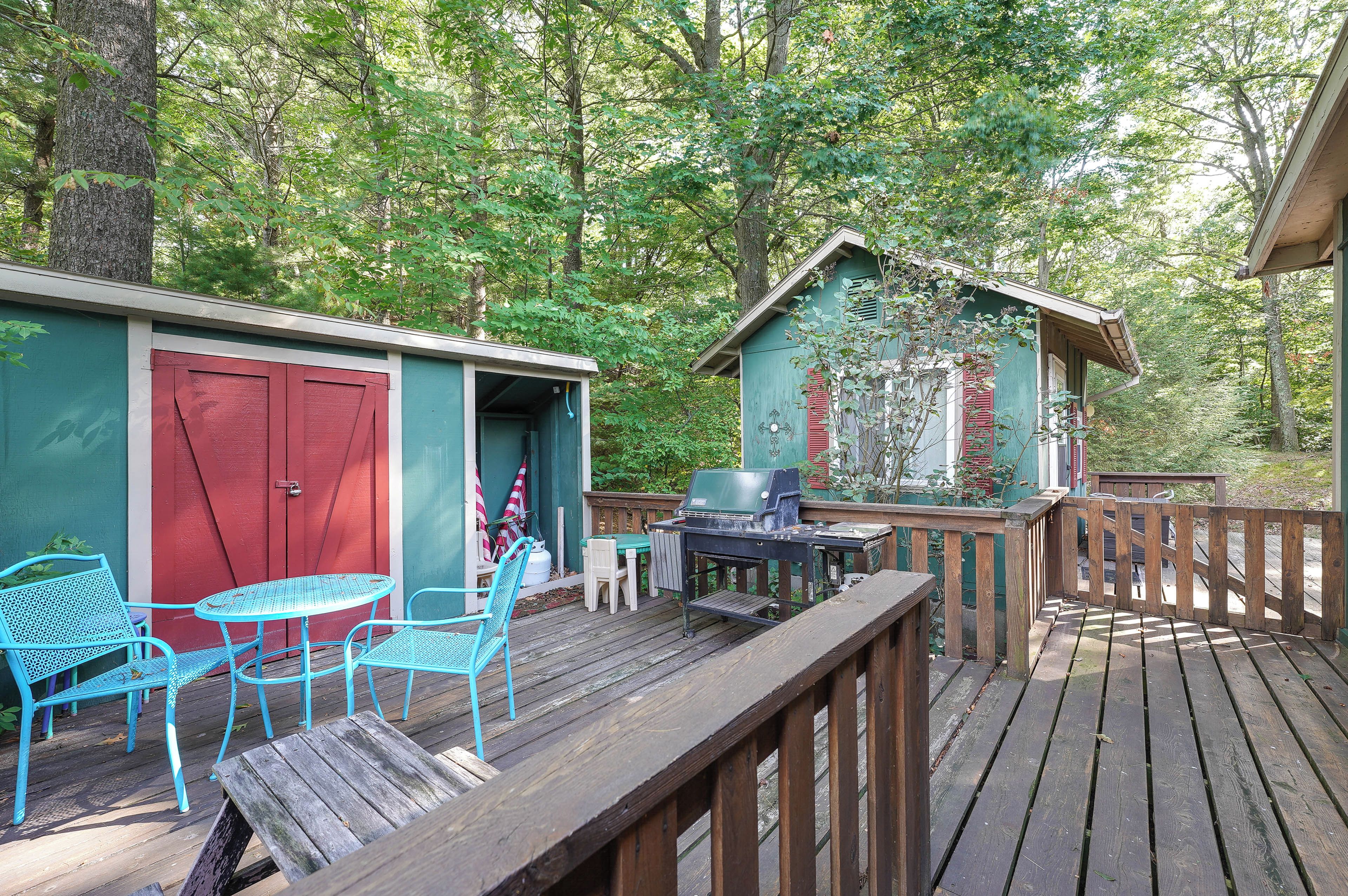 A wooden deck with outdoor seating, a barbecue grill, and a small shed with a red door.