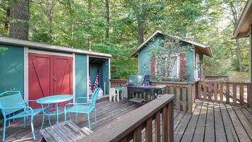 A wooden deck with outdoor seating, a barbecue grill, and a small shed with a red door.