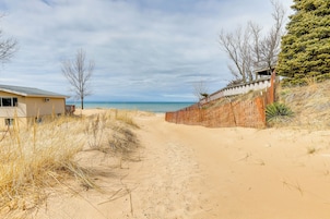Un sendero arenoso que lleva a la playa, con una valla de madera a un lado y un edificio al otro.