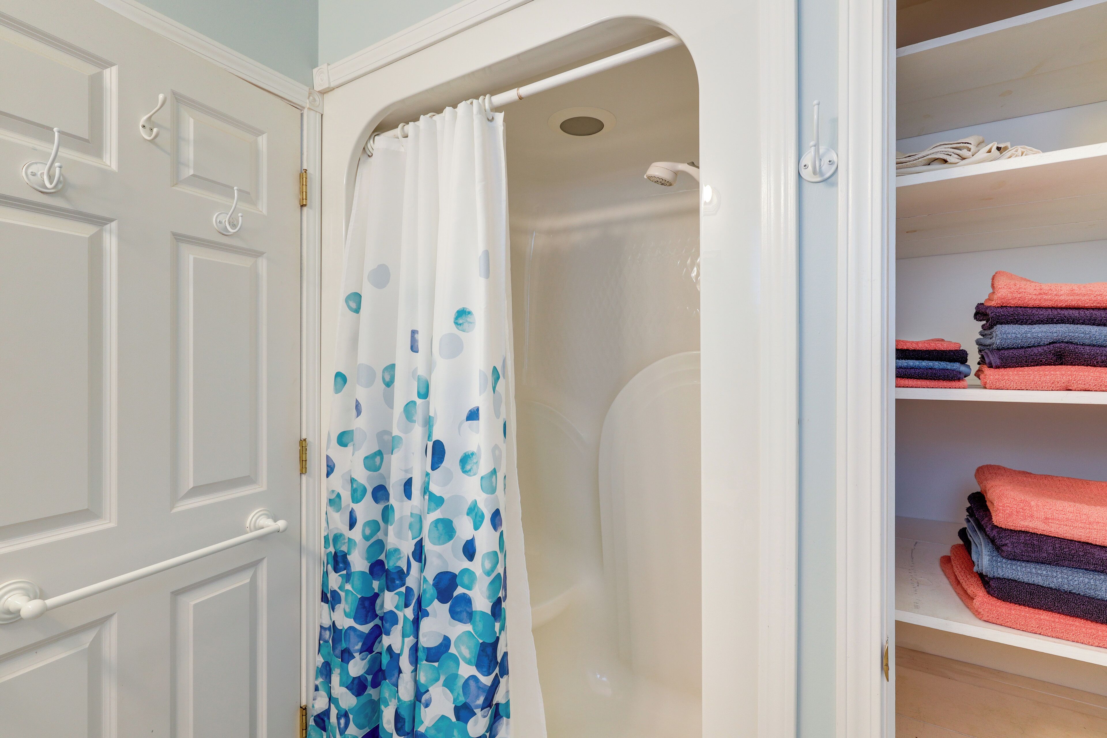 A bathroom with a shower, a white door with a towel rack, and shelves with folded towels.