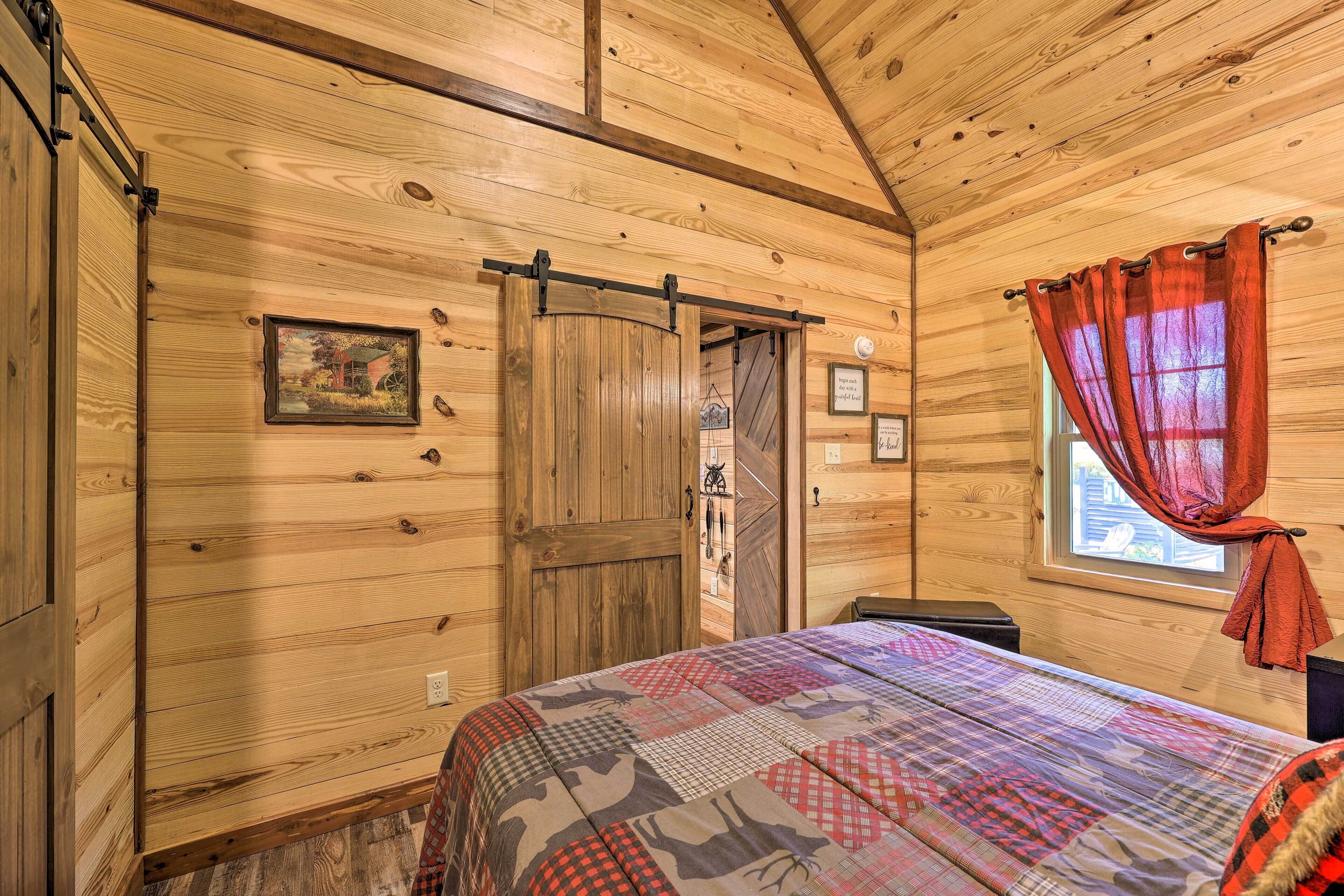 A wooden cabin room with a bed, a window with curtains, and a door with a barn door style.