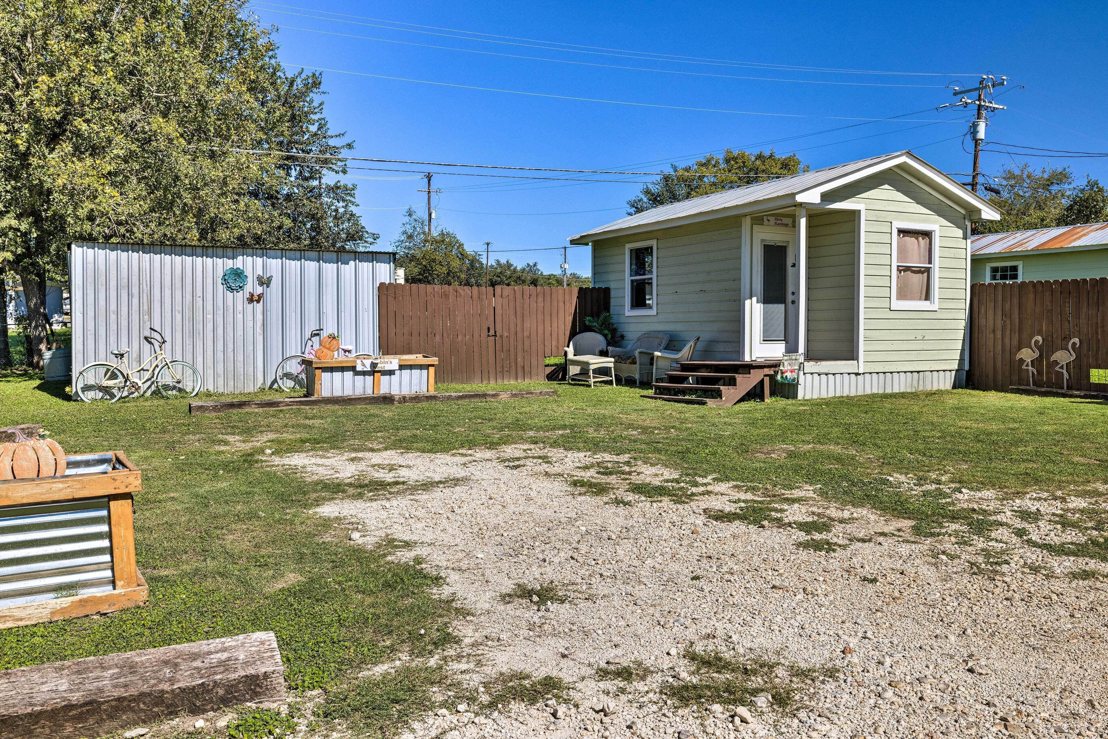 A small, single-story house with a front porch, a covered patio area, and a fenced backyard.