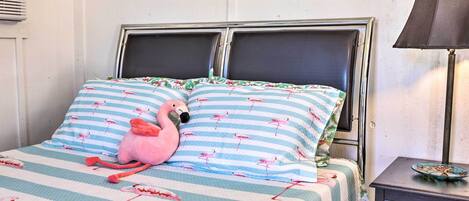Una cama con ropa de cama a rayas y un peluche de flamenco rosa.