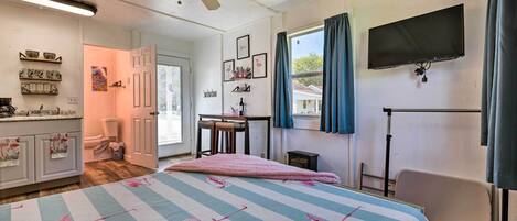 A bedroom with a bed, a ceiling fan, a TV, and a window with curtains.