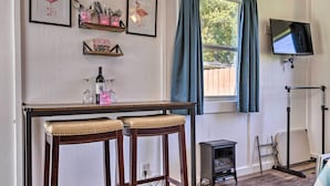 A room with a wooden table, two barstools, a small heater, a TV mounted on the wall, and a window with curtains. - Flirty Flamingo' Studio: 1 Mi to Canyon Lake (Canyon Lake)