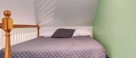 A bedroom with a bed, a wooden headboard, a white radiator, and a green wall.