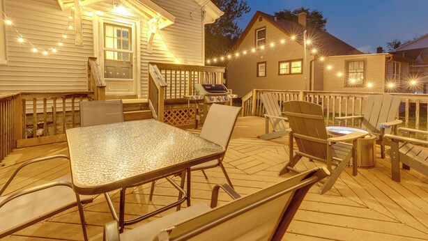 A wooden deck with a glass-top table and chairs, a grill, and string lights.