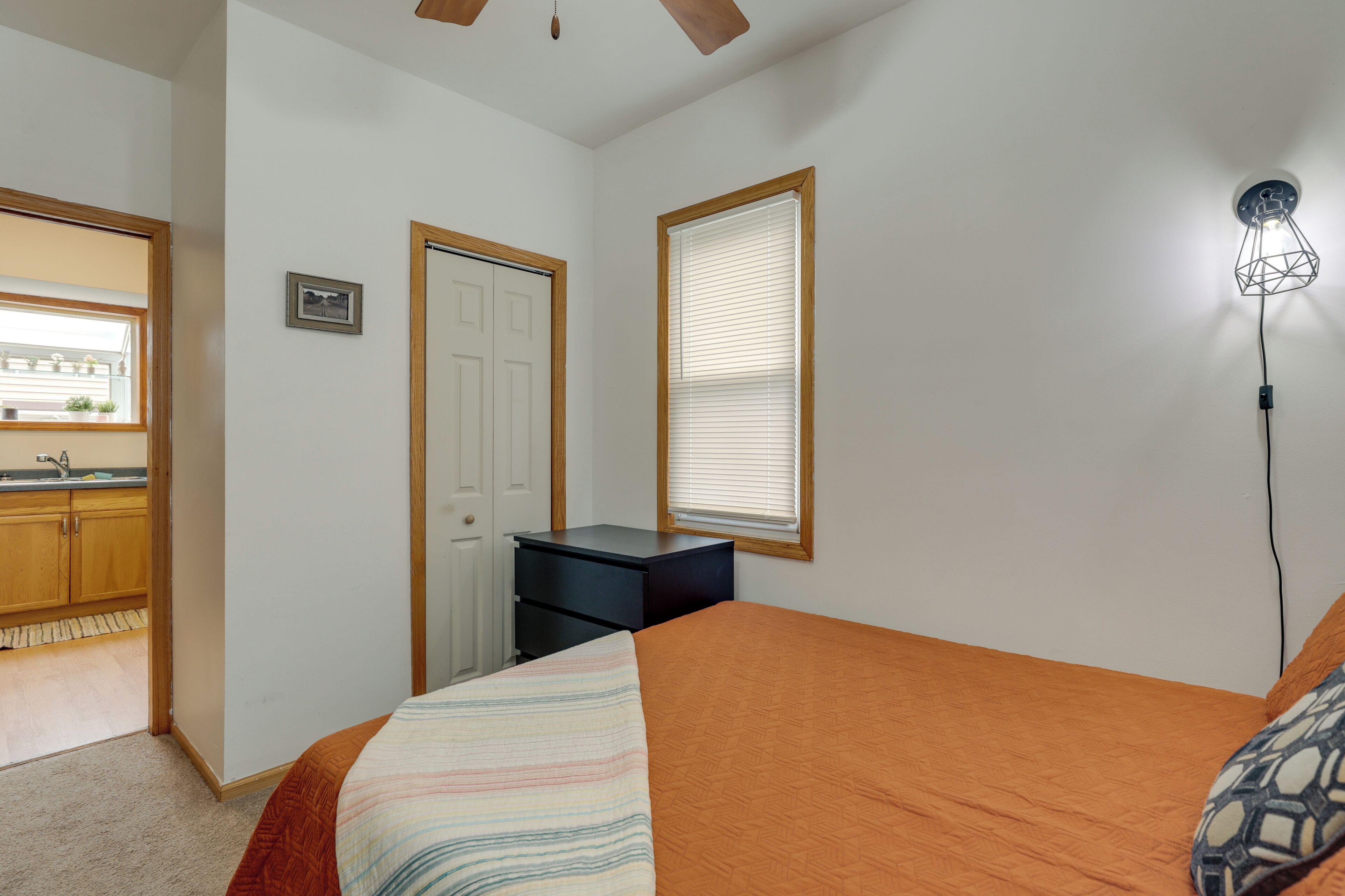 A bedroom with a bed, a desk, a chair, a window with blinds, and a ceiling fan.