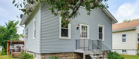 A two-story house with a stone foundation, a front porch, and a small staircase leading to the entrance.