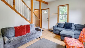 A living room with two grey sofas, a wooden staircase, and a door leading outside.