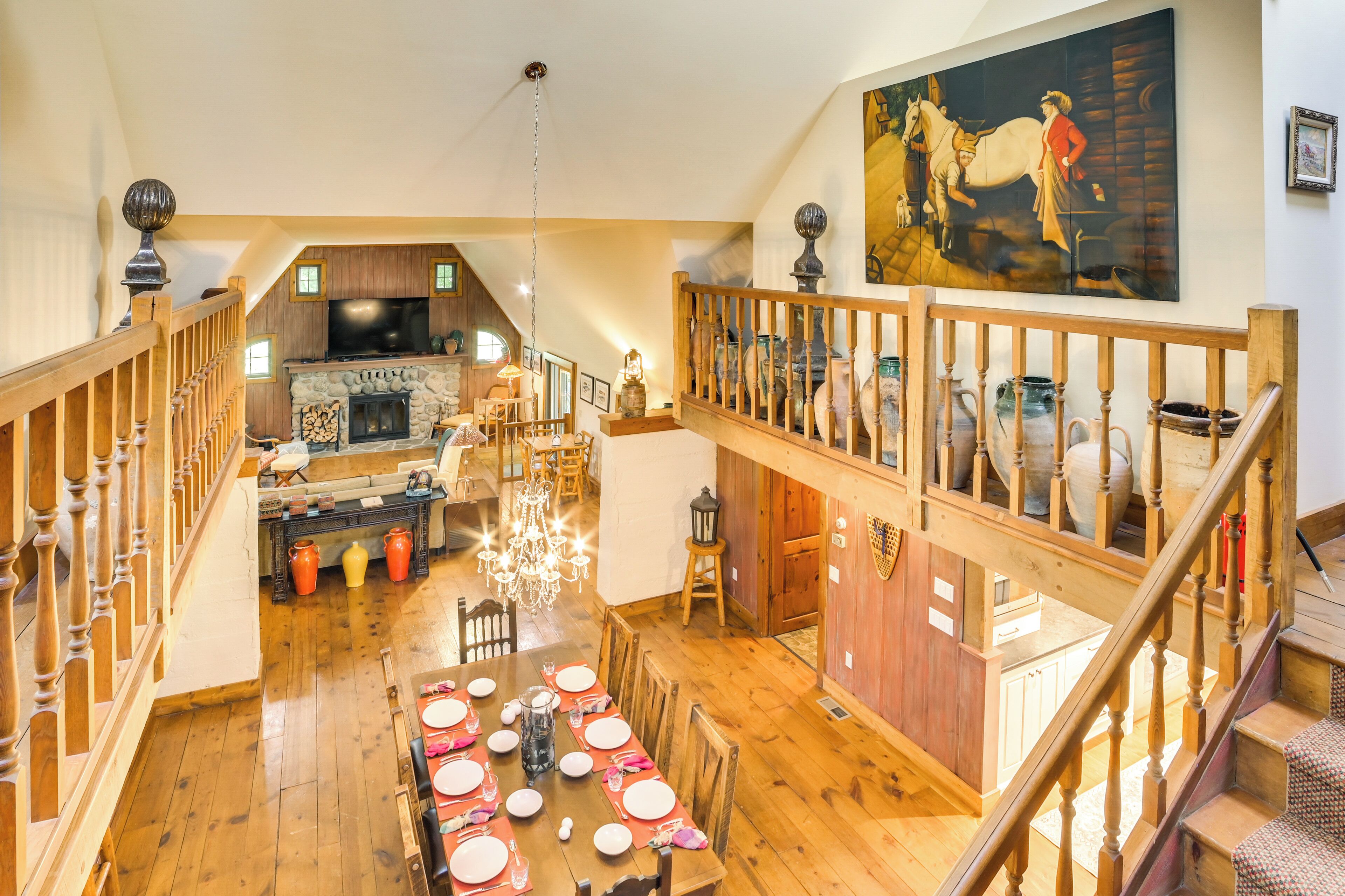 A spacious loft-style living area with a high ceiling, wooden flooring, a dining table set for six, and a fireplace.