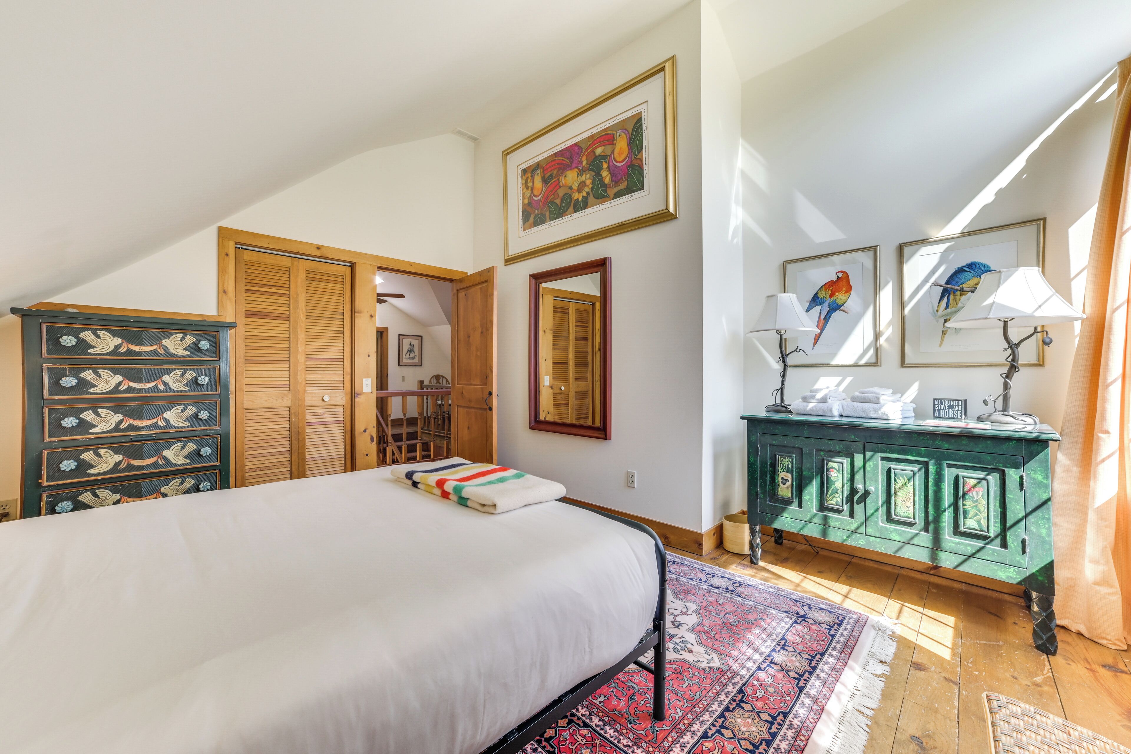 A bedroom with a bed, a dresser, a mirror, and a painting on the wall.