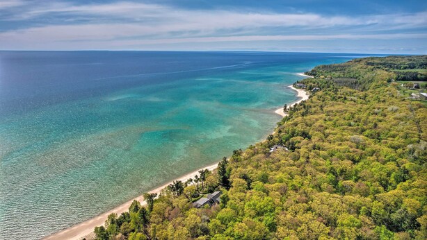 Une vue aérienne d’une zone côtière avec une plage, une végétation luxuriante et une mer bleue et limpide.