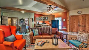 A spacious living room with a wooden ceiling, a brown leather sofa, a red armchair, and a wooden coffee table with books and a candle. - Dog-friendly Ranch Cottage w/ Yard ~ 13 Mi to Bend (Bend)