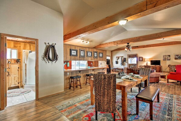 A spacious living area with a wooden ceiling, a dining table with chairs, a red armchair, and a television.