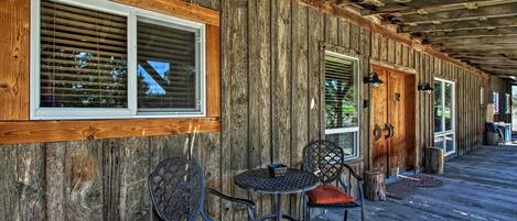 A wooden exterior with a covered porch, two tables with chairs, and a wooden door.