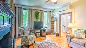 A living room with a fireplace, a television, a ceiling fan, and a large window with curtains. - Historic 'hammond House' w/ Wine Country View! (Strasburg)