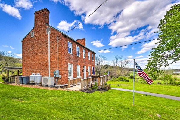 A red brick house with a porch, a flagpole with an American flag, and a grassy yard.
