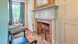 A bathroom with a bathtub, a window with curtains, a fireplace with a mirror above it, and a wooden floor. - Historic 'hammond House' w/ Wine Country View! (Strasburg)