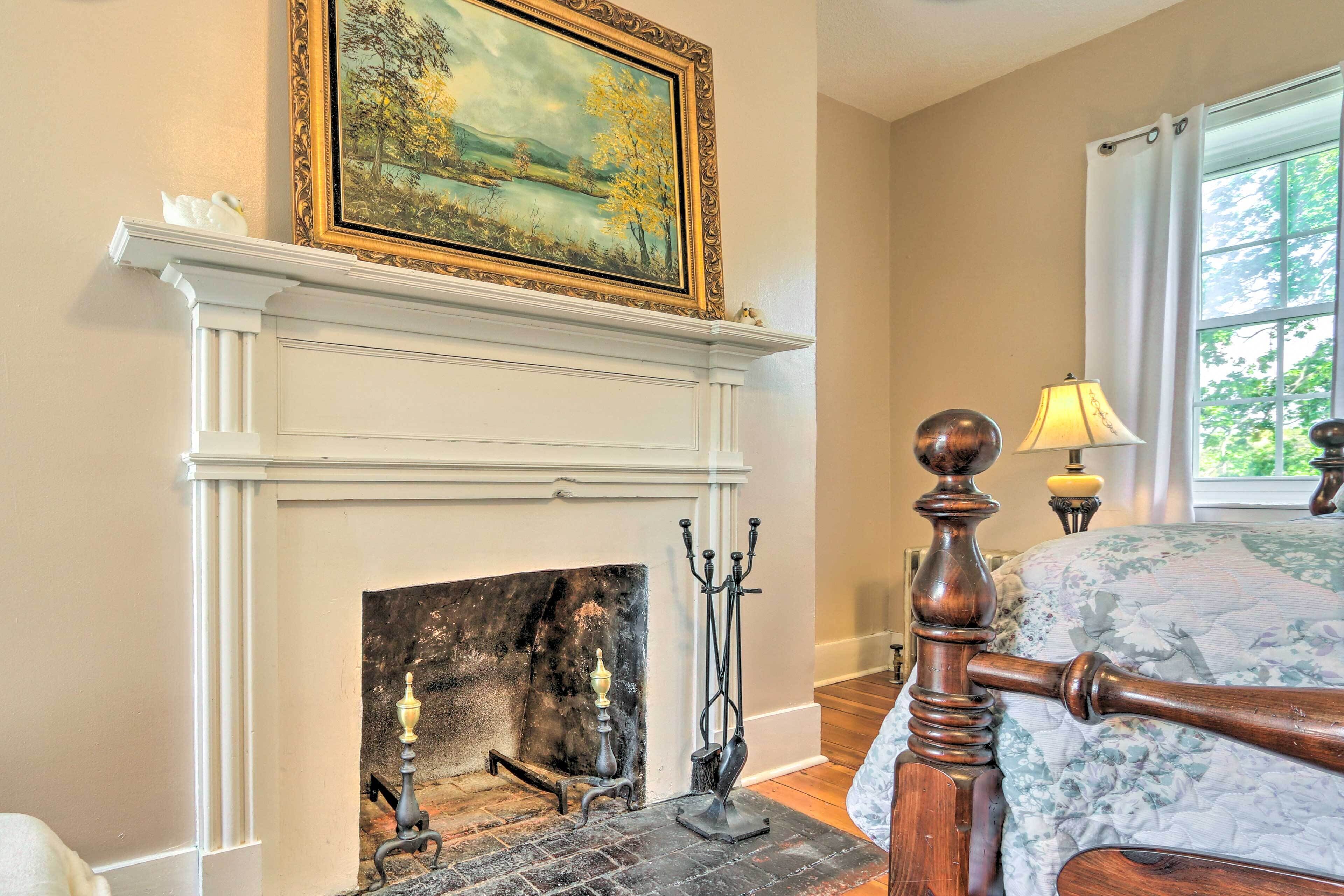 A room with a fireplace, a bed with a floral bedspread, and a window with a view of greenery.